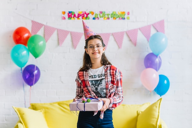 Foto gratuita ritratto di ragazza felice che indossa cappello di partito tenendo il regalo di compleanno