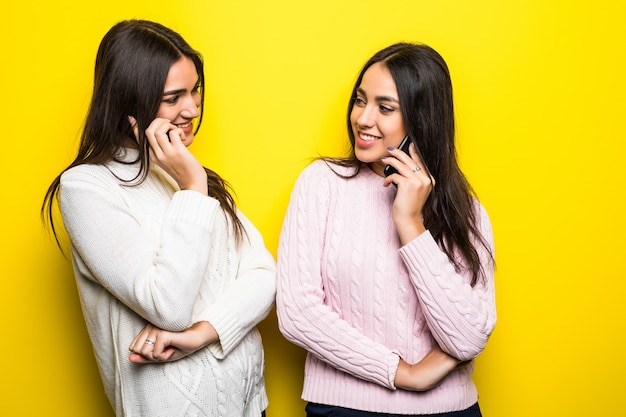 Portrait of a happy girls talking on mobile phones isolated over yellow wall