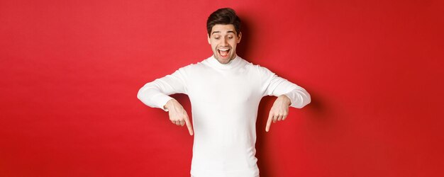 Portrait of happy goodlooking man pointing fingers down and looking at advertisement with excited sm...