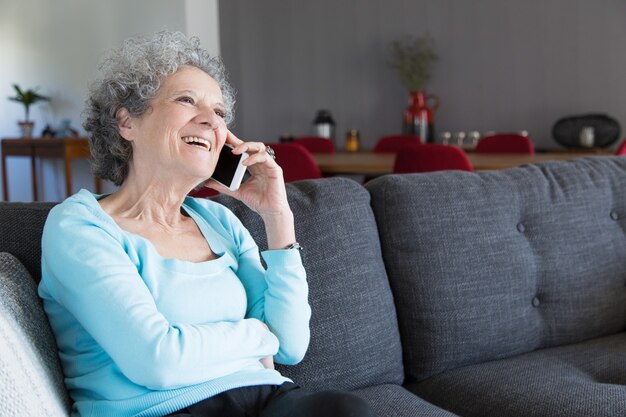 Portrait of happy grandma sitting on sofa and talking on phone