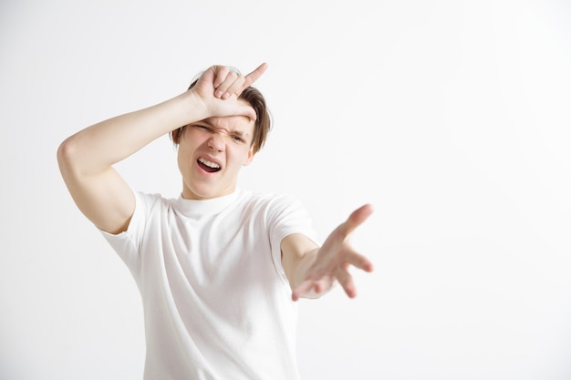 Portrait of happy guy showing loser sign over forehead and smiling in cause of victory and laughing