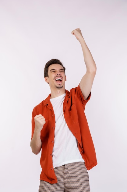 Portrait of happy joyful young man standing doing winner gesture clenching fists keeping isolated on white color wall background studio