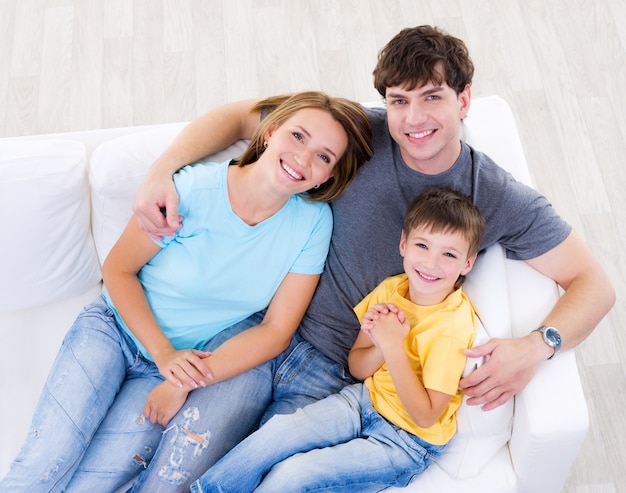 Ritratto di giovane famiglia che ride felice con il figlio in casuals sul divano di casa - angolo alto