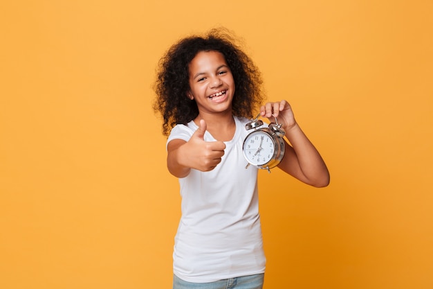 Portrait of a happy little african girl holding alarm clock