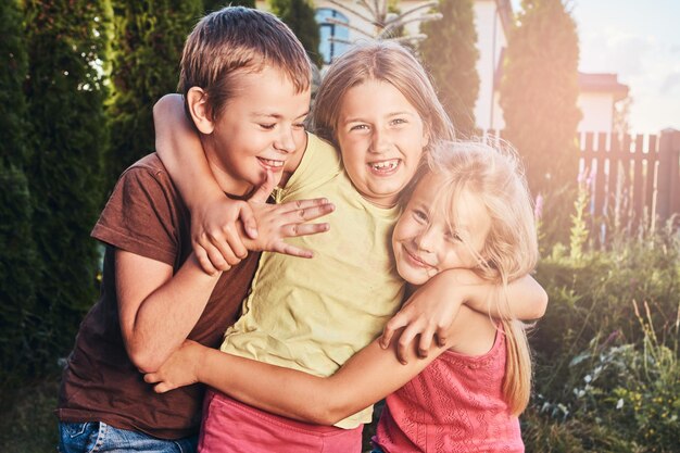 Портрет счастливых маленьких друзей, веселящихся во дворе. Три милых маленьких друга обнимаются и играют.