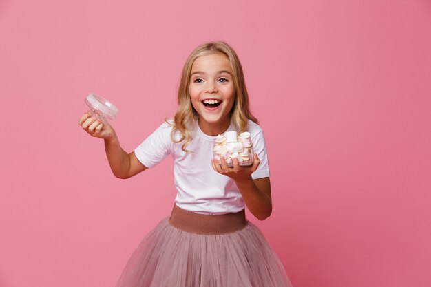 Portrait of a happy little girl holding open jar of marshmallow