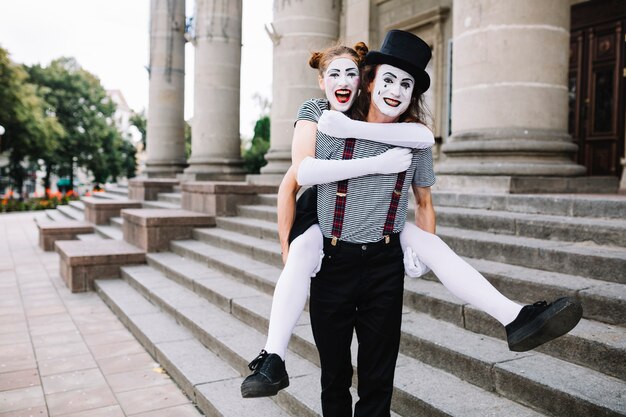 Portrait of a happy male mime giving piggyback ride to female mime