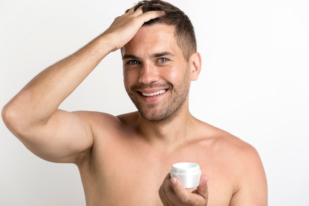 Portrait of happy man applying hair wax standing against white background