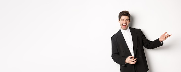 Free photo portrait of happy man dancing at party playing on invisible guitar and laughing standing in black su