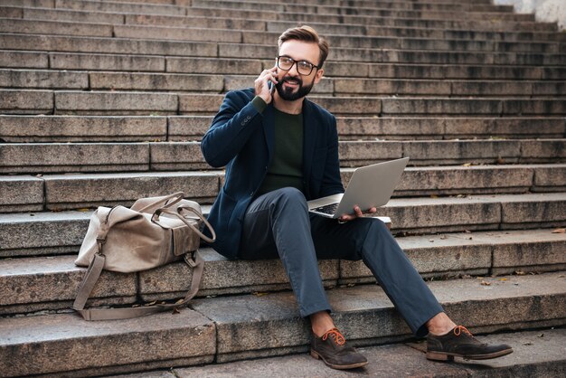 Portrait of a happy man in eyeglasses working on laptop