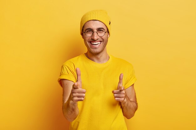 Portrait of happy man points fore fingers at camera, chooses you, looks gladfully at camera, smiles broadly