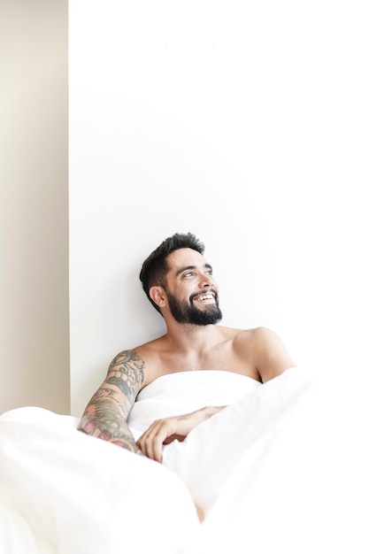 Foto gratuita ritratto di un uomo felice seduto sul letto guardando lontano