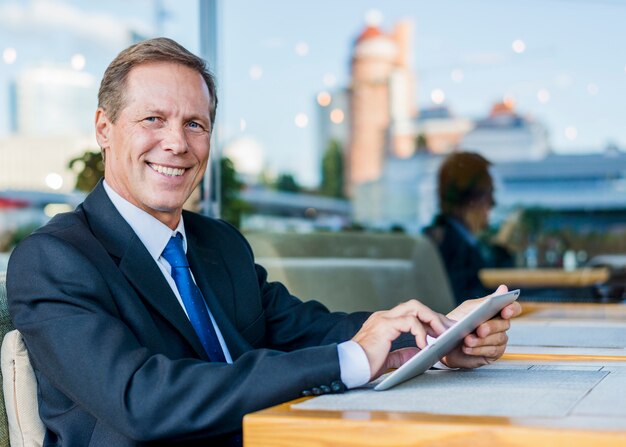 Portrait of a happy mature businessman using digital tablet in restaurant