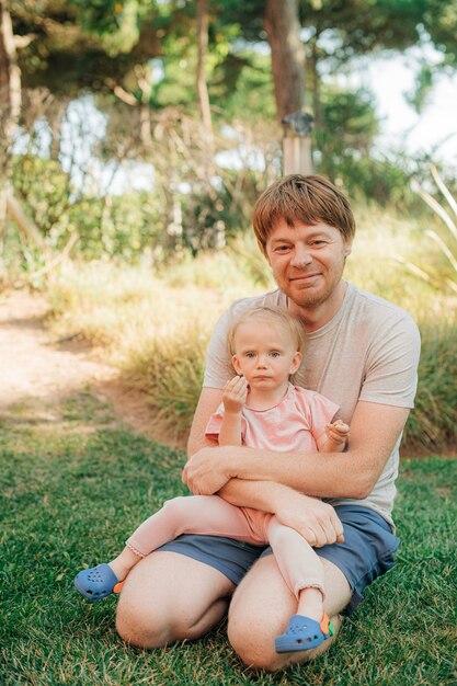 Portrait of happy mid adult man with baby daughter sitting on grass