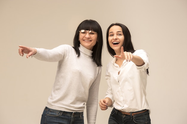 portrait of a happy mother and daughter at studio on gray background. Human positive emotions and facial expressions concept