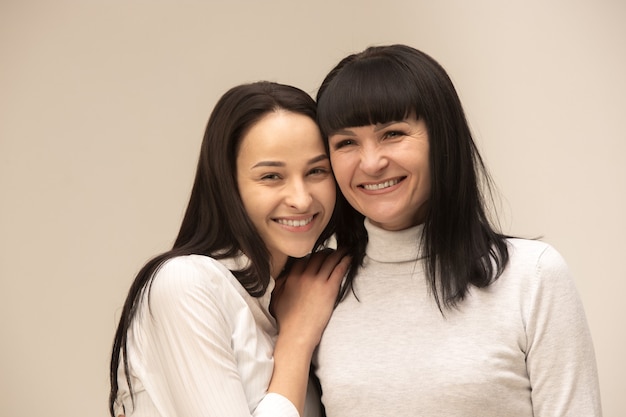 A portrait of a happy mother and daughter at studio on gray background. Human positive emotions and facial expressions concept