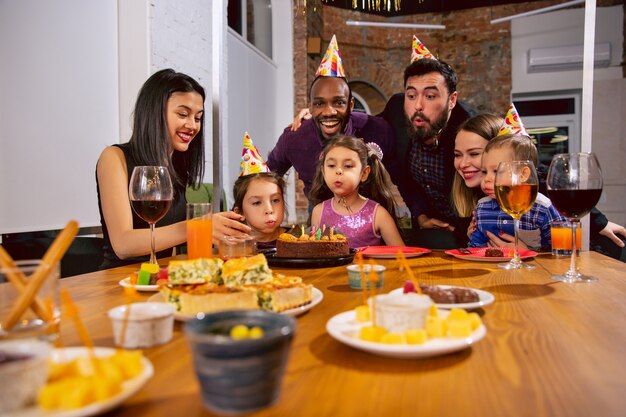 自宅で誕生日を祝う幸せな多民族家族の肖像画。あいさつや楽しい子供たちと一緒におやつを食べたり、ワインを飲んだりする大家族。お祝い、家族、パーティー、家のコンセプト。