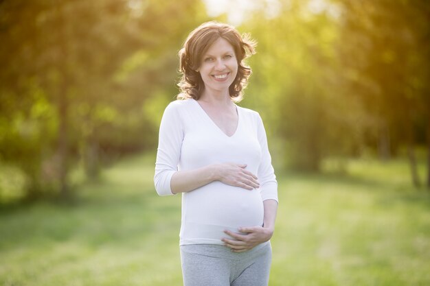 Portrait of happy pregnant female walking in park