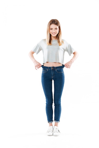 Portrait of a happy satisfied young woman standing and showing her weight loss isolated