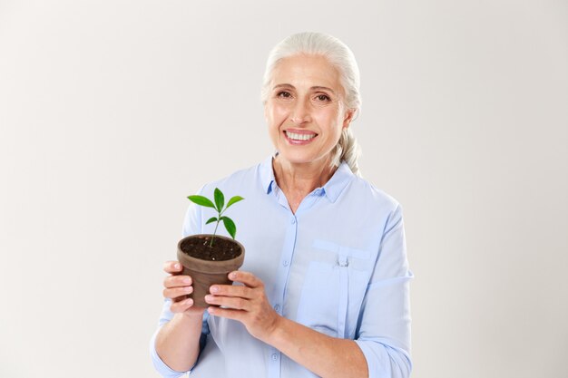 Portrait of happy senior woman, holding pot with green plant