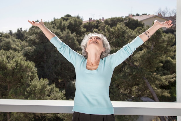 Portrait of happy senior woman standing with raised arms