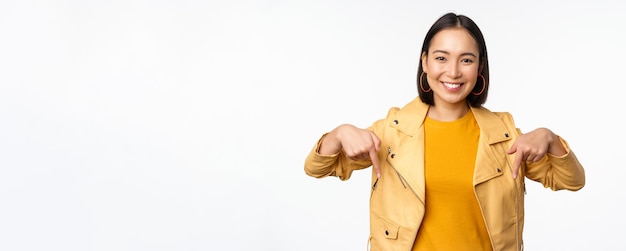 Portrait of happy smiling asian girl pointing fingers down and showing logo demonstrating banner sta