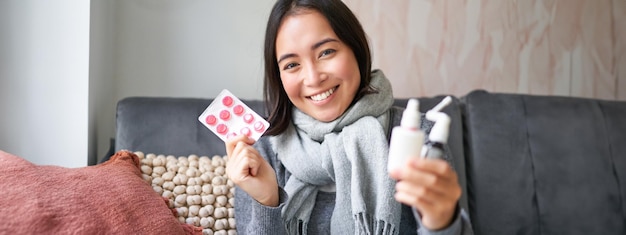 Portrait of happy smiling asian girl showing medication sore throat spray and drugs from flu or cold