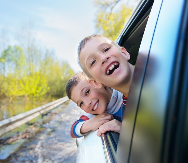 Portrait of happy smiling boys looks out the car window.