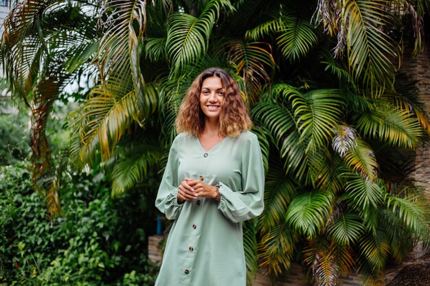 Portrait of happy smiling european tanned woman with short curly hair in summer romantic long sleeve dress dress outside villa