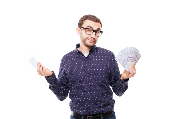 Portrait of a happy smiling man in glasses holding bunch of money banknotes and showing credit card isolated over white wall