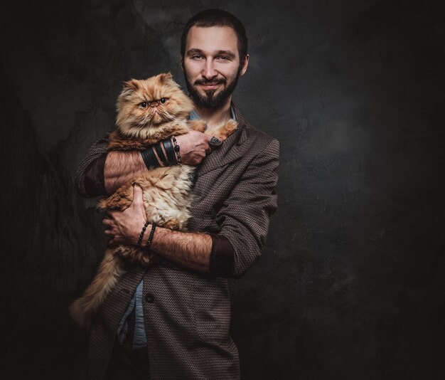 어두운 사진 스튜디오에서 크고 푹신한 고양이와 함께 행복한 웃는 남자의 초상화.