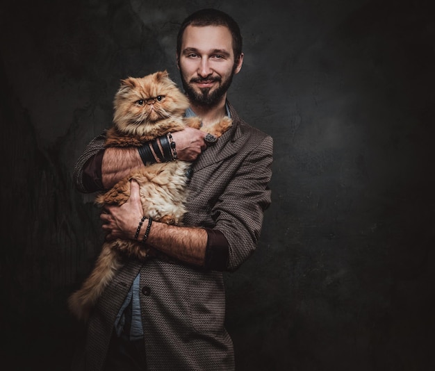 Портрет счастливого улыбающегося мужчины с большой и пушистой кошкой в темной фотостудии.
