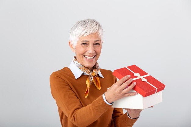 회색 배경 위에 격리된 선물 상자를 여는 행복한 웃는 성숙한 여성의 초상화 선물 상자를 들고 있는 흥분된 캐주얼 여성
