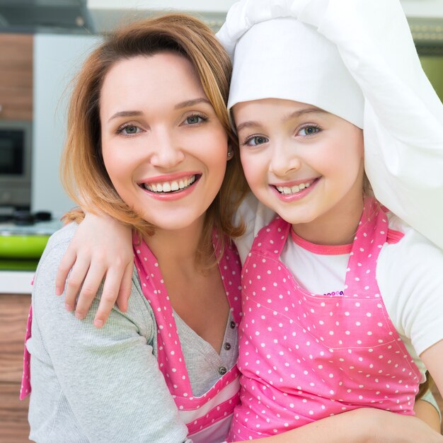 Portrait of happy smiling mother and daughter in pink apron at the kitchen