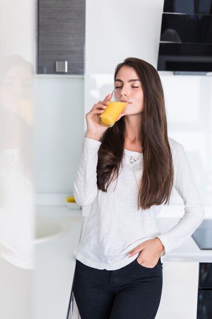 Портрет счастливой улыбающейся женщины, пьющей свежий апельсиновый сок на кухне