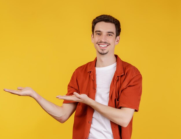 Portrait of happy smiling young man presenting and showing your text or product isolated on yellow background