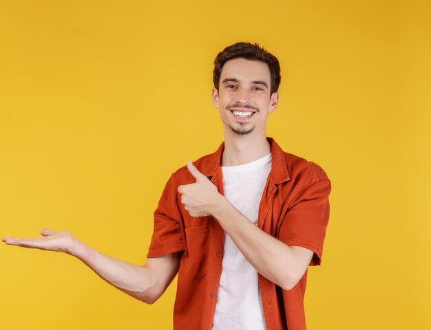 Портрет счастливого улыбающегося молодого человека, представляющего и показывающего ваш текст или продукт на желтом фоне