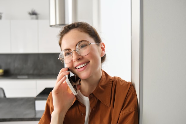 Foto gratuita ritratto di una giovane donna felice e sorridente a casa che parla al telefono cellulare chiamando un amico e facendo una bella cosa