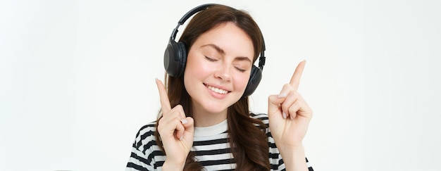 Portrait of happy student girl listening music in headphones dancing and pointing fingers at copy