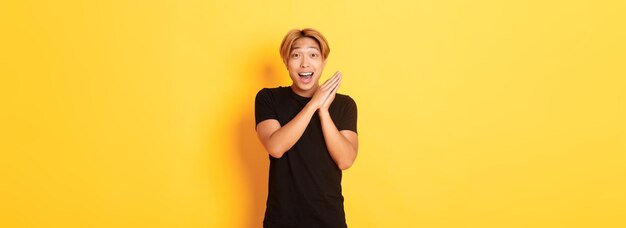 Portrait of happy and surprised asian man clap hands and smiling delighted standing yellow backgroun