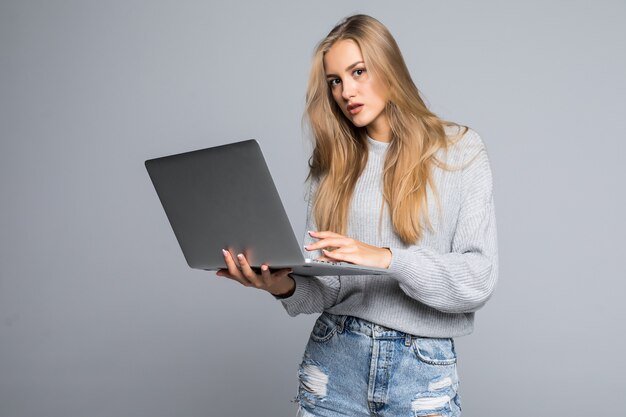 Портрет счастливой удивленной женщины, стоящей с ноутбуком, изолированной на сером фоне