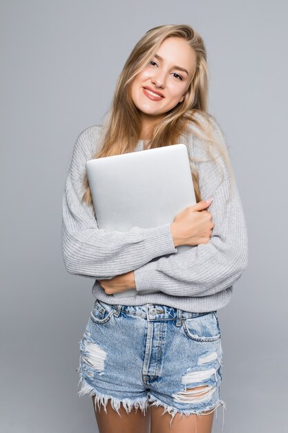 Портрет счастливой удивленной женщины, стоящей с ноутбуком, изолированной на сером фоне