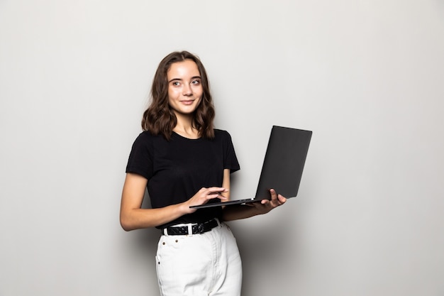 Portrait of happy surprised woman standing with laptop isolated on gray wall
