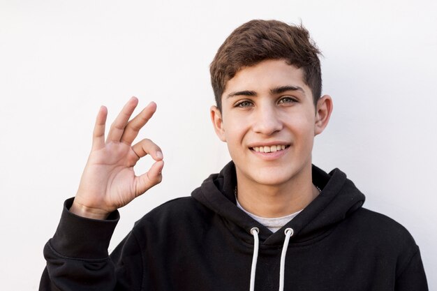 Portrait of happy teenage boy showing ok gesture on white background
