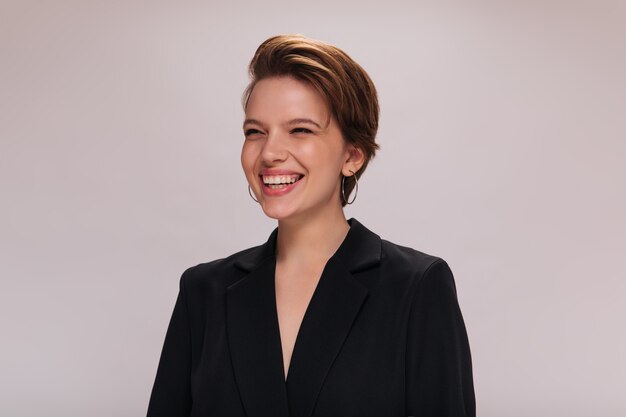 Portrait of happy woman in black jacket. Happy short-haired girl in dark suit widely and sincerely smiles on isolated background