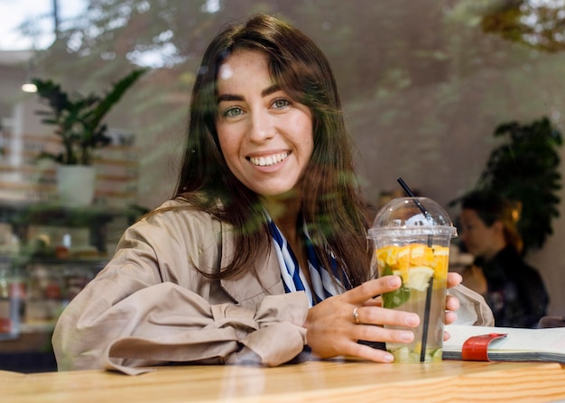 Free photo portrait of happy woman in cafe with fresh lemonade and headphones