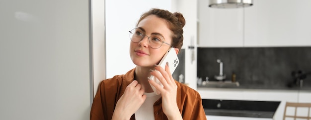 Foto gratuita ritratto di una donna felice a casa che risponde a una chiamata telefonica parlando sul cellulare con in mano uno smartphone e sorridendo