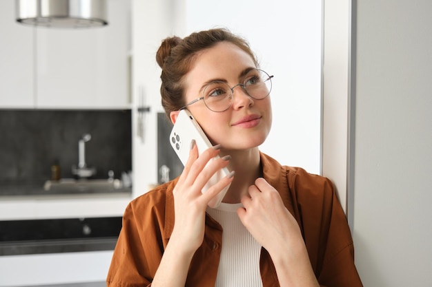 スマートフォンを握り,笑顔で携帯電話で話す電話に答える家にいる幸せな女性の肖像画