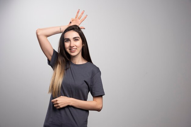 Portrait of happy woman posing and putting bunny ears over gray background.