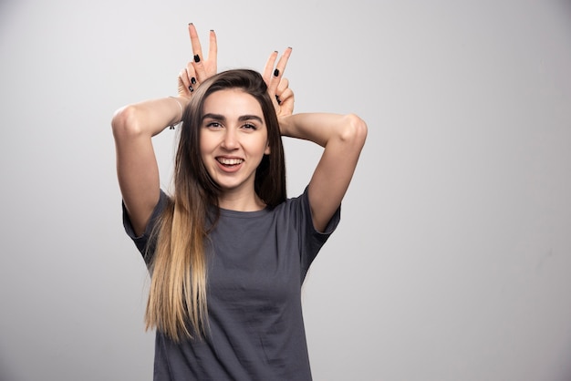 Portrait of happy woman posing and putting bunny ears over gray background.